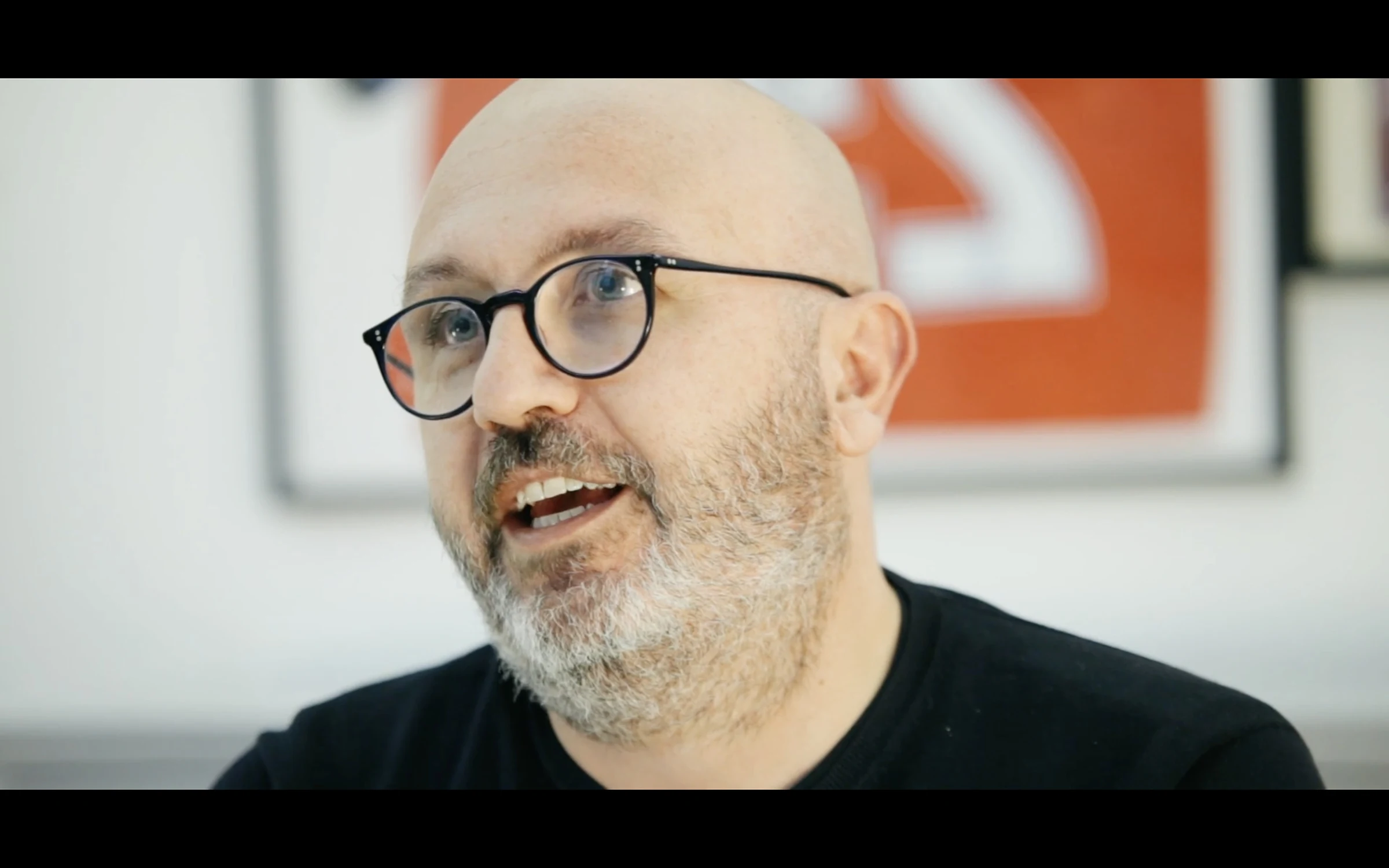 A designer speaking animatedly in front of a red and white poster