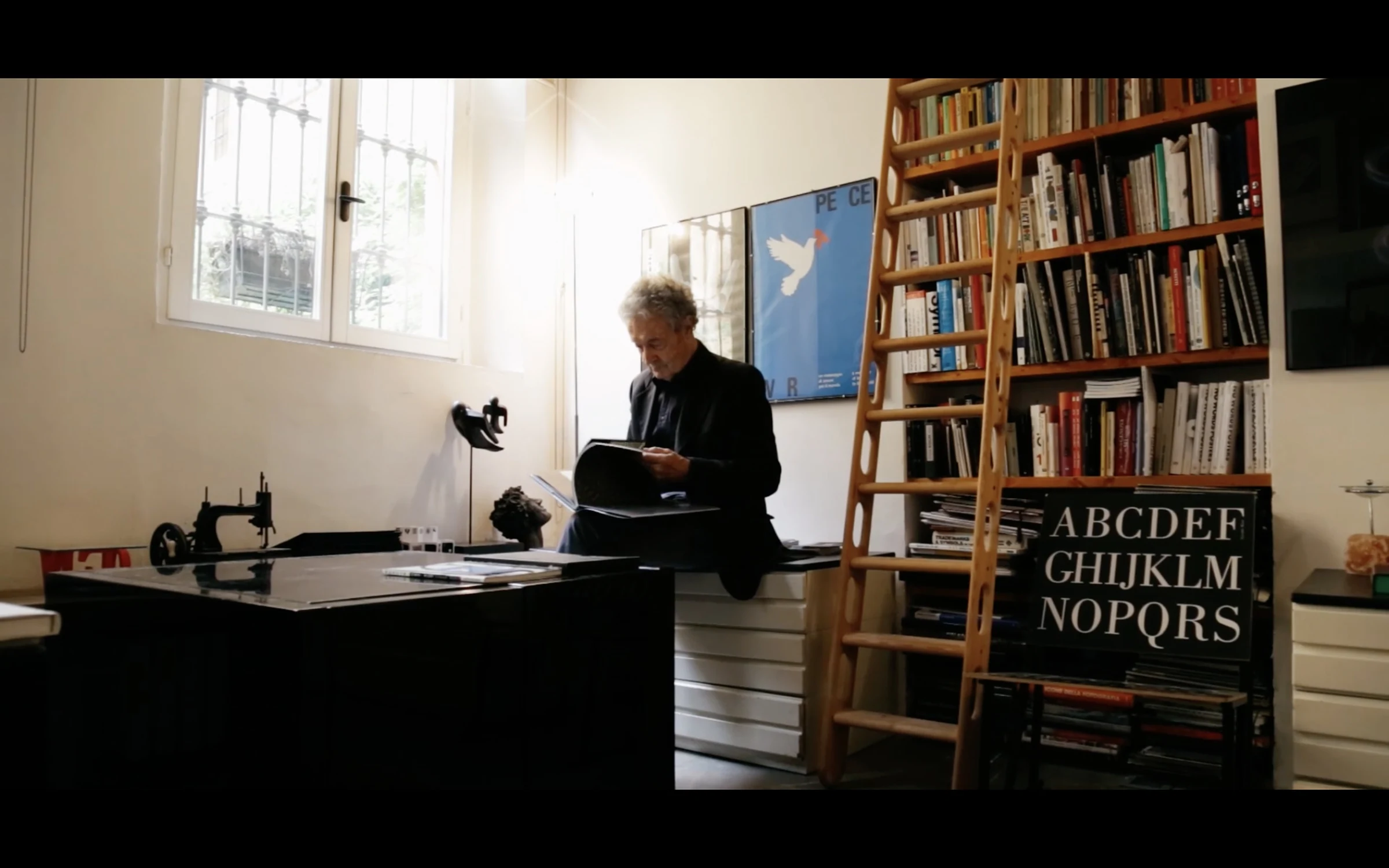 A figure reading at a desk in a library, an alphabet chart on the wall