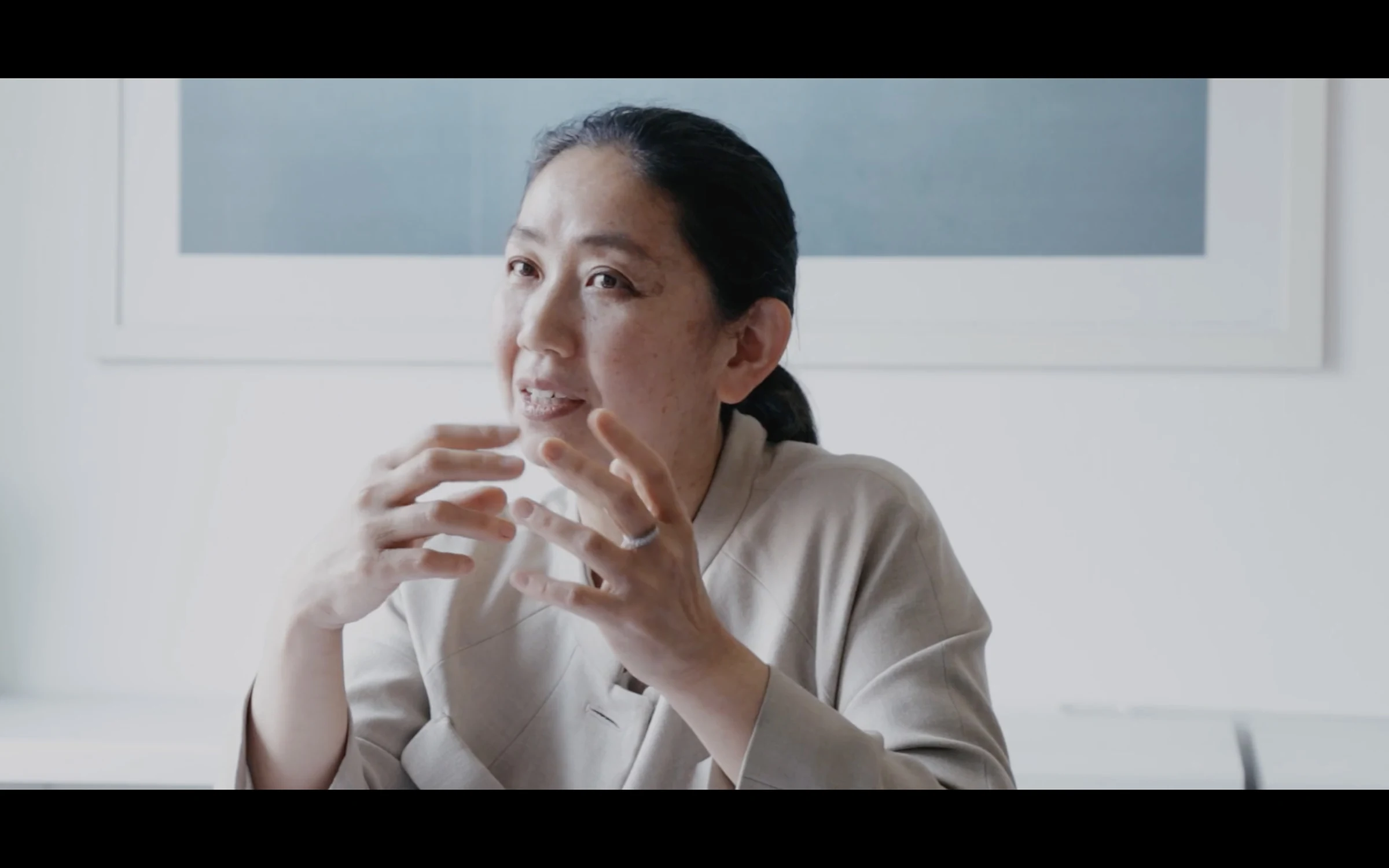 A woman seated in thought before a framed print, mid-interview