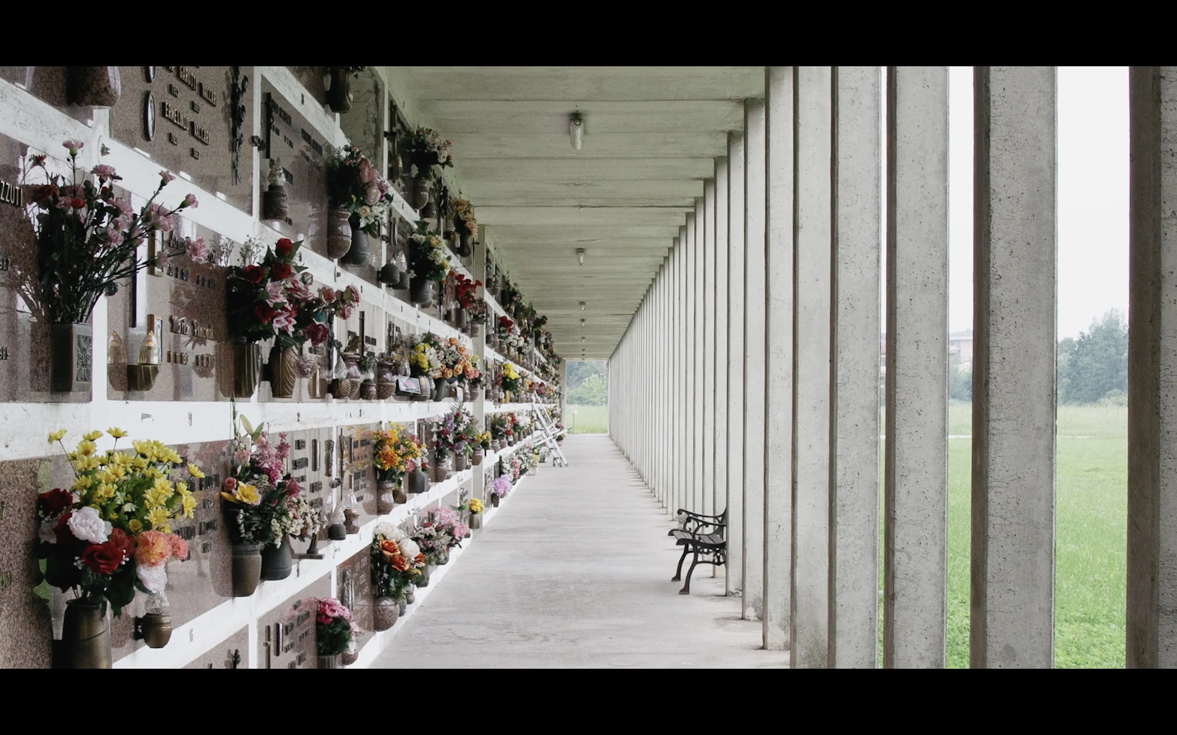 A colonnaded cemetery corridor lined with flowers and memorial plaques